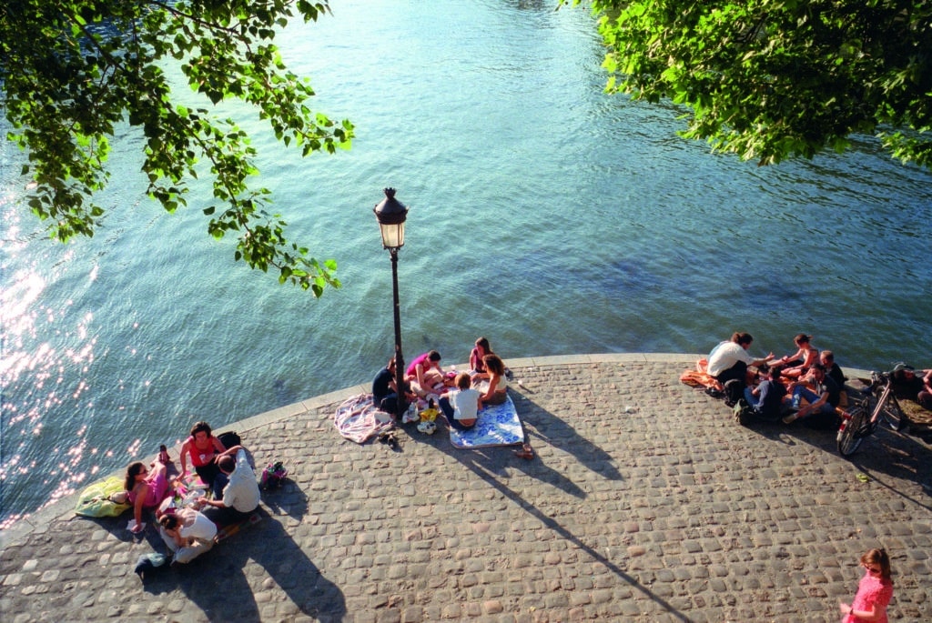 people sitting in groups beside the River Seine in Paris