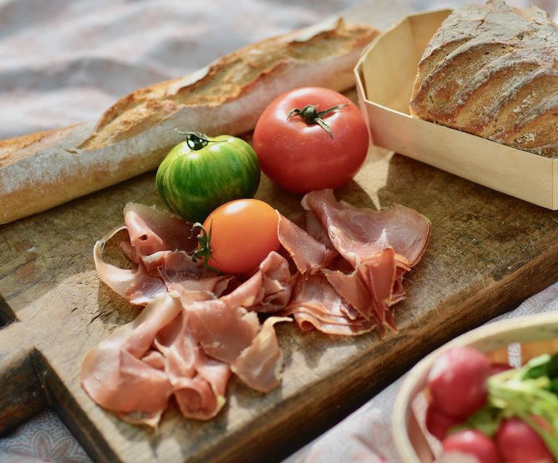 serrano ham, colored tomatoes and a baguette laid out on a board