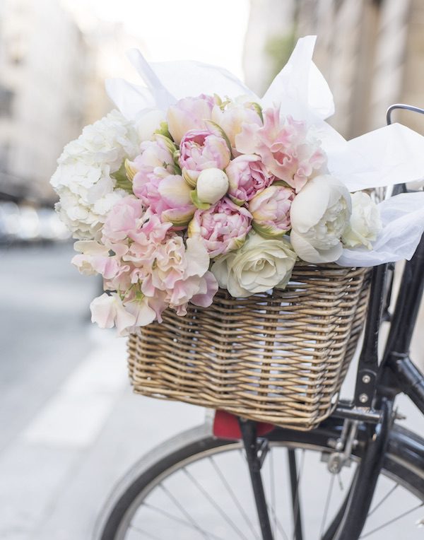 a basket of roses and peonies in a bike basket