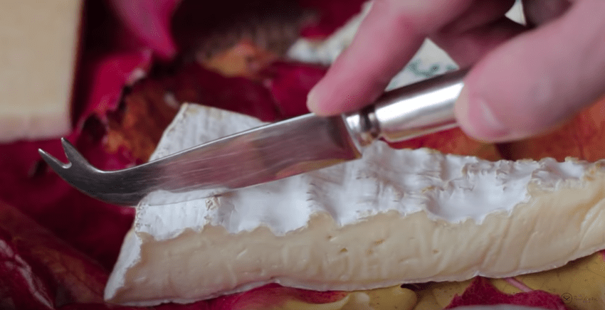 a knife slicing into a hunk of brie cheese