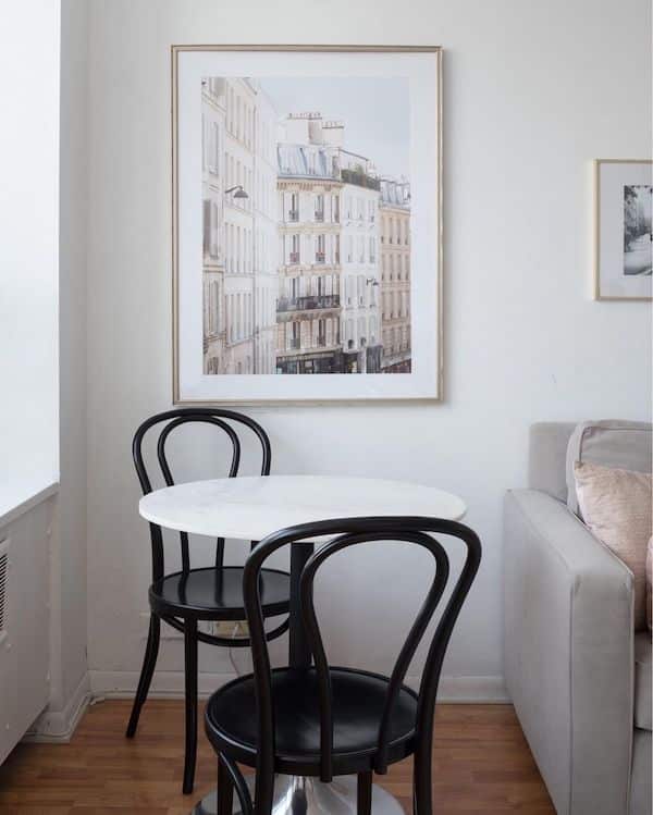 circle table with two black chairs and  a hanging print of Paris